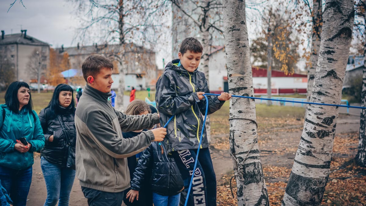 Kids enjoying an outdoor rope activity among birch trees during fall.